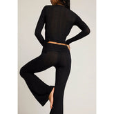 Person wearing a black long-sleeve top and black pants with a cutout design on a light background